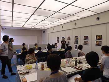 フレスコ画体験教室で多数の参加者が講師から説明を受けている様子の写真